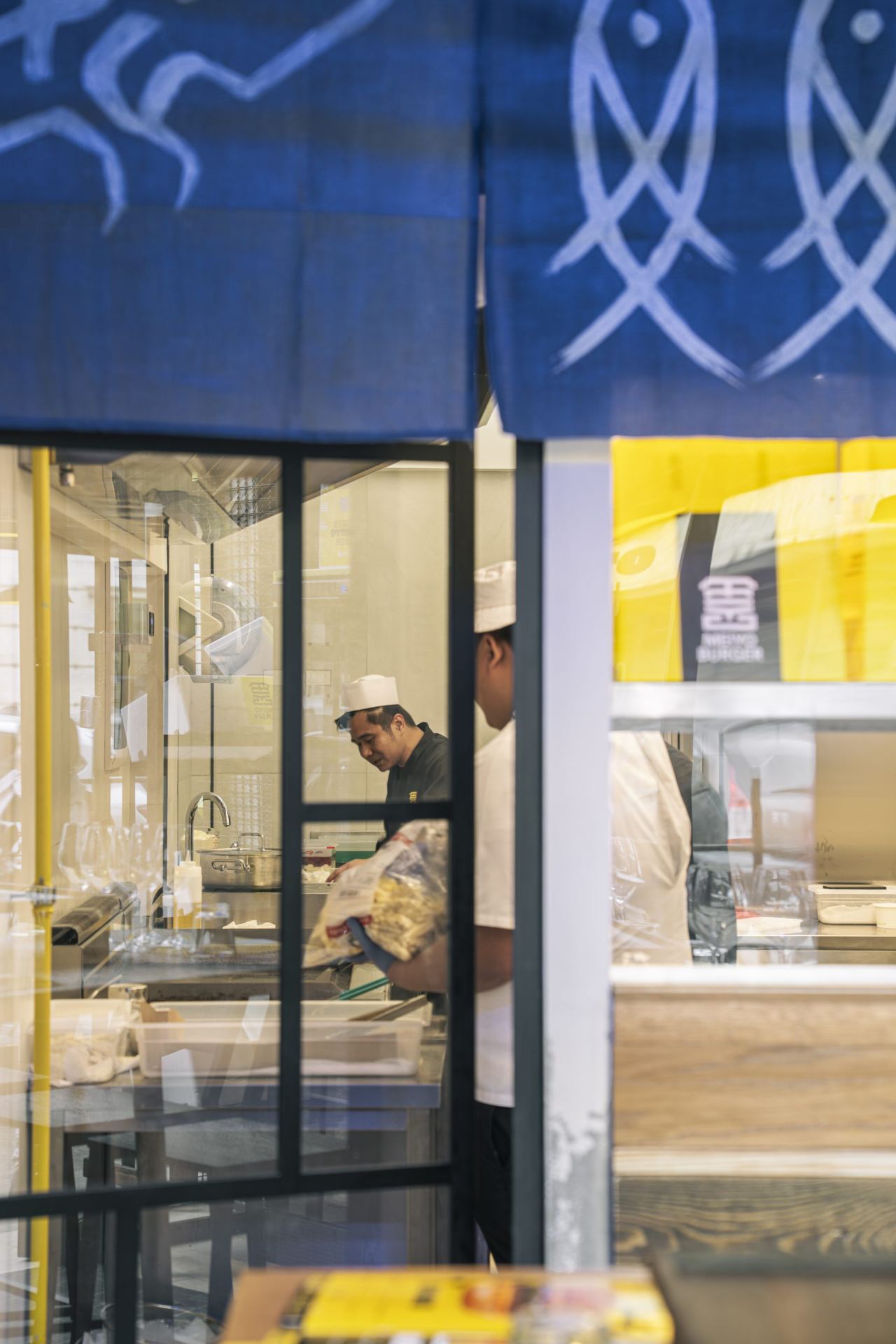 Chef al pass dietro il noren blu con pesci disegnati a mano